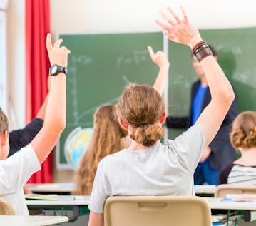 4 alumnos con las manos en alto para responder a la pregunta del profesor