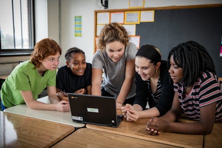 Four smiling students looking at the screen of a laptop computer.