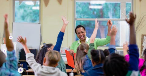 Teacher and students smiling and raising their hand in classroom